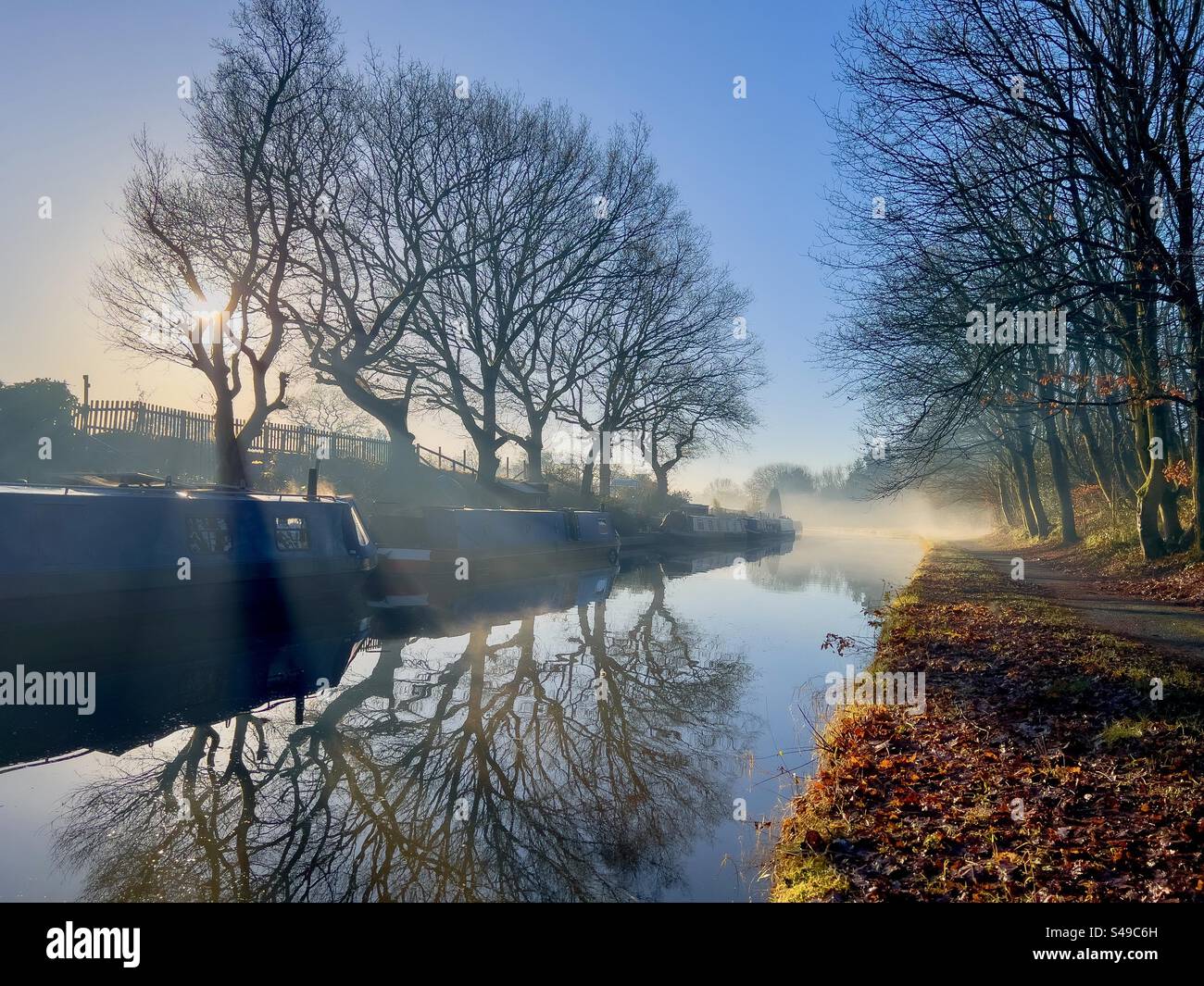 Reflections of narrow boats and trees in canal on a sunny but misty winter morning. The Leeds and Liverpool canal at Adlington near Chorley in Lancashire. - Smartphone Captured Stock Image