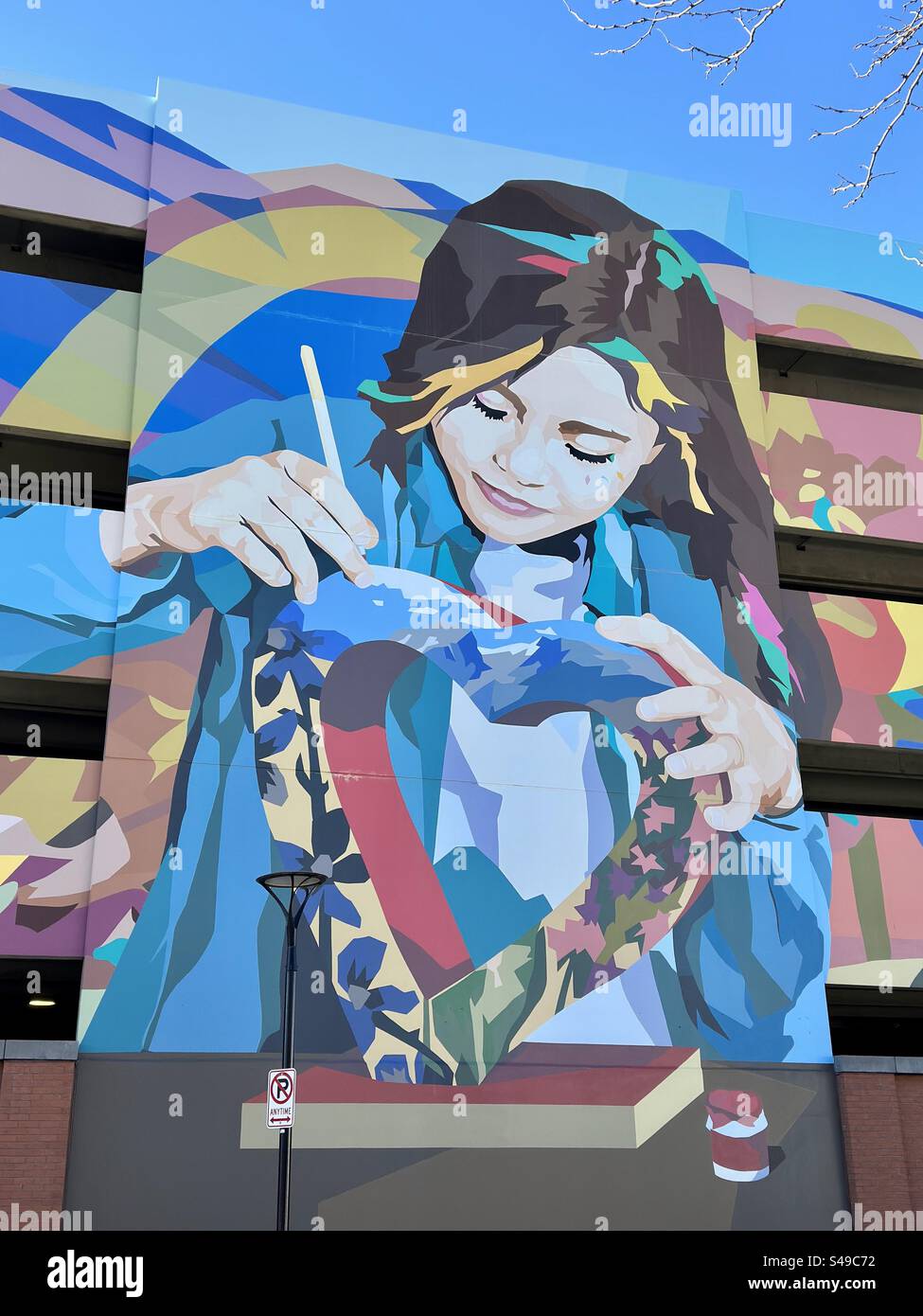 Wall mural of a female painting on a heart-shaped object. Exterior of parking garage in downtown Loveland, Colorado, USA. Colorful artwork. - Smartphone Captured Stock Image