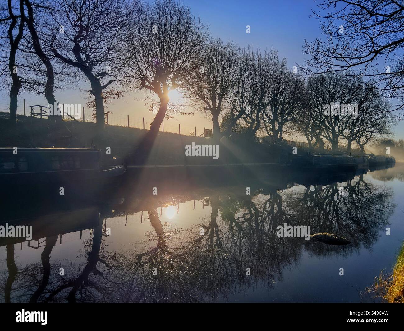 Sunny and misty winter morning with trees and narrow boats reflected in the canal. Leeds and Liverpool canal at Adlington near Chorley in Lancashire. - Smartphone Captured Stock Image