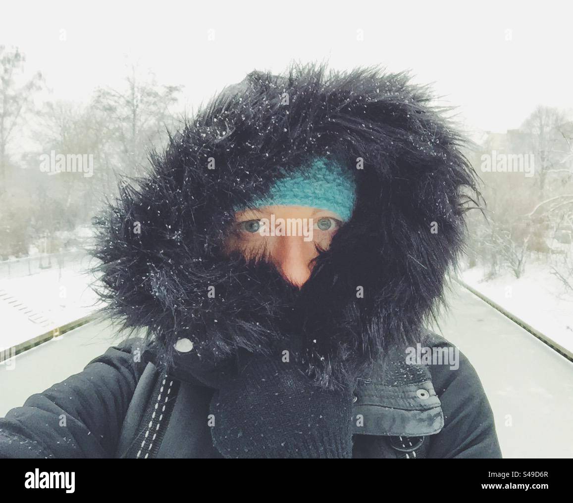Snowy winter selfie wearing a blue knit hat and hood with fur. - Smartphone Captured Stock Image