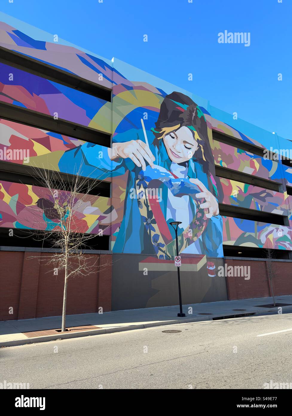 Loveland, Colorado, USA: View of parking garage in downtown area with mural on the side.  Colorful building with multiple levels. Tree and street light in front. - Smartphone Captured Stock Image