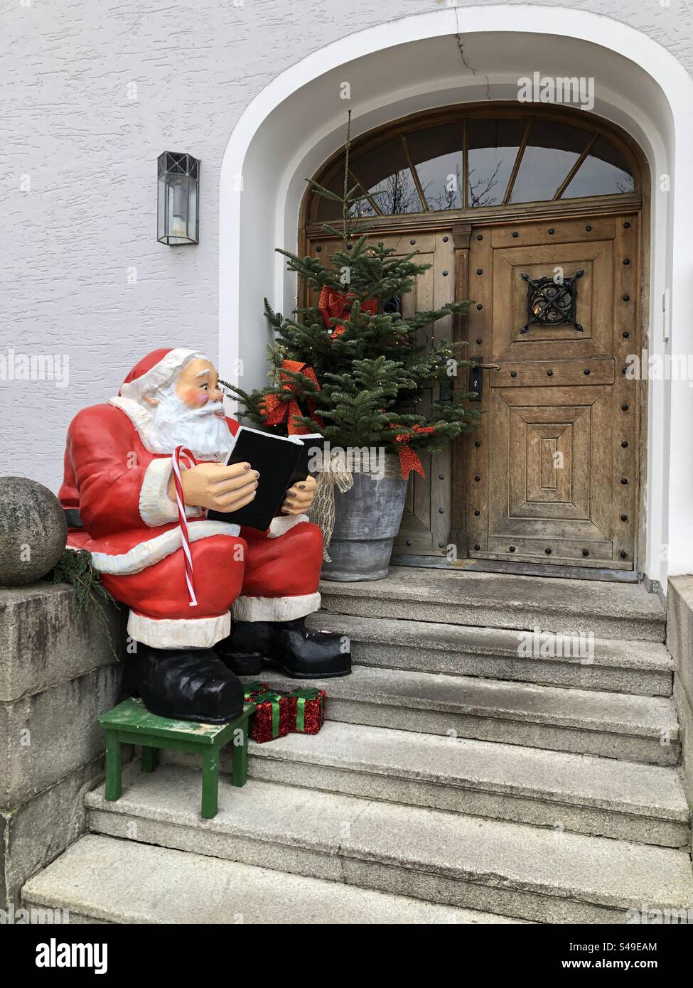 Santa Claus figure sitting on a staircase in front of an old wooden entrance door Stock Photo