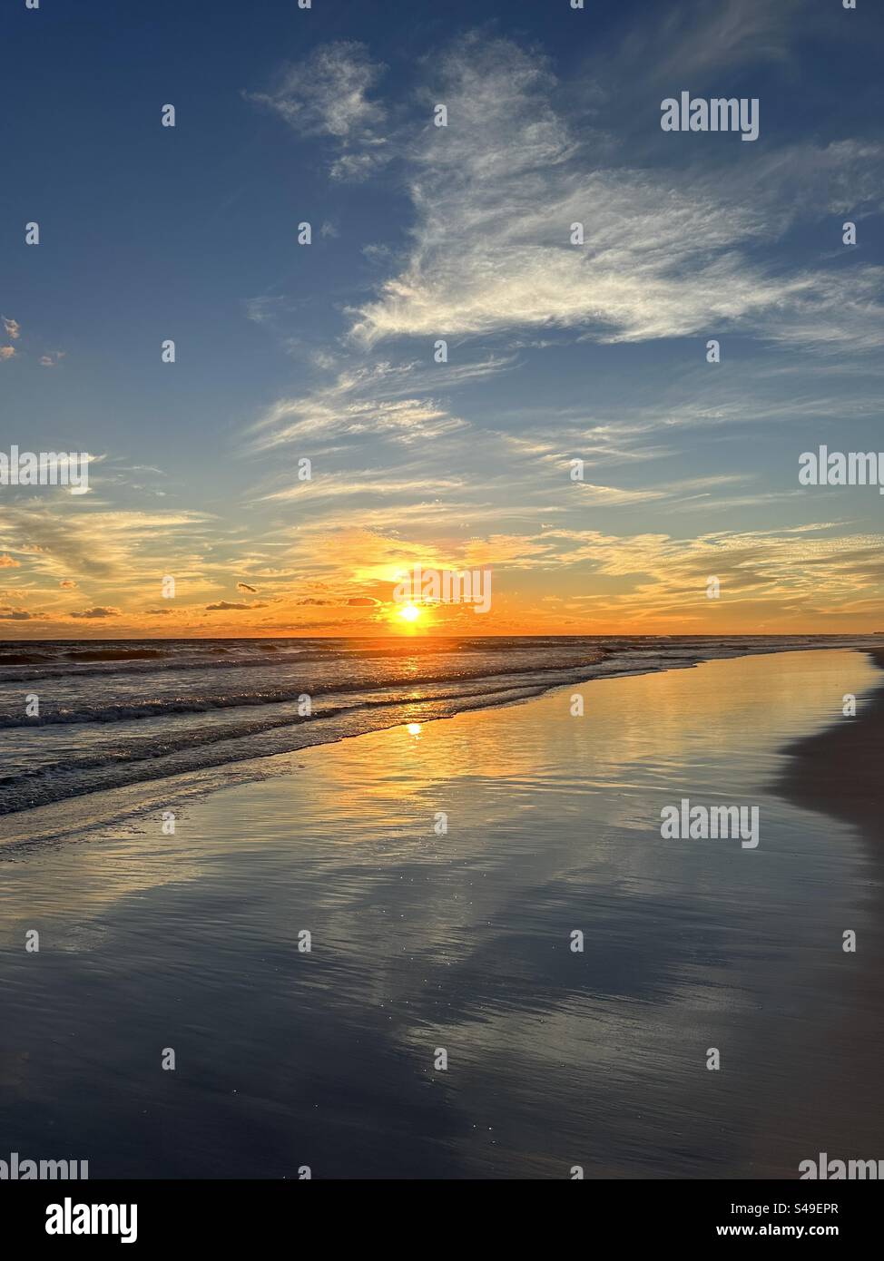 Golden sun setting over the Gulf of Mexico with clouds and colors reflecting onto the sand in Miramar Beach Florida - Smartphone Captured Stock Image