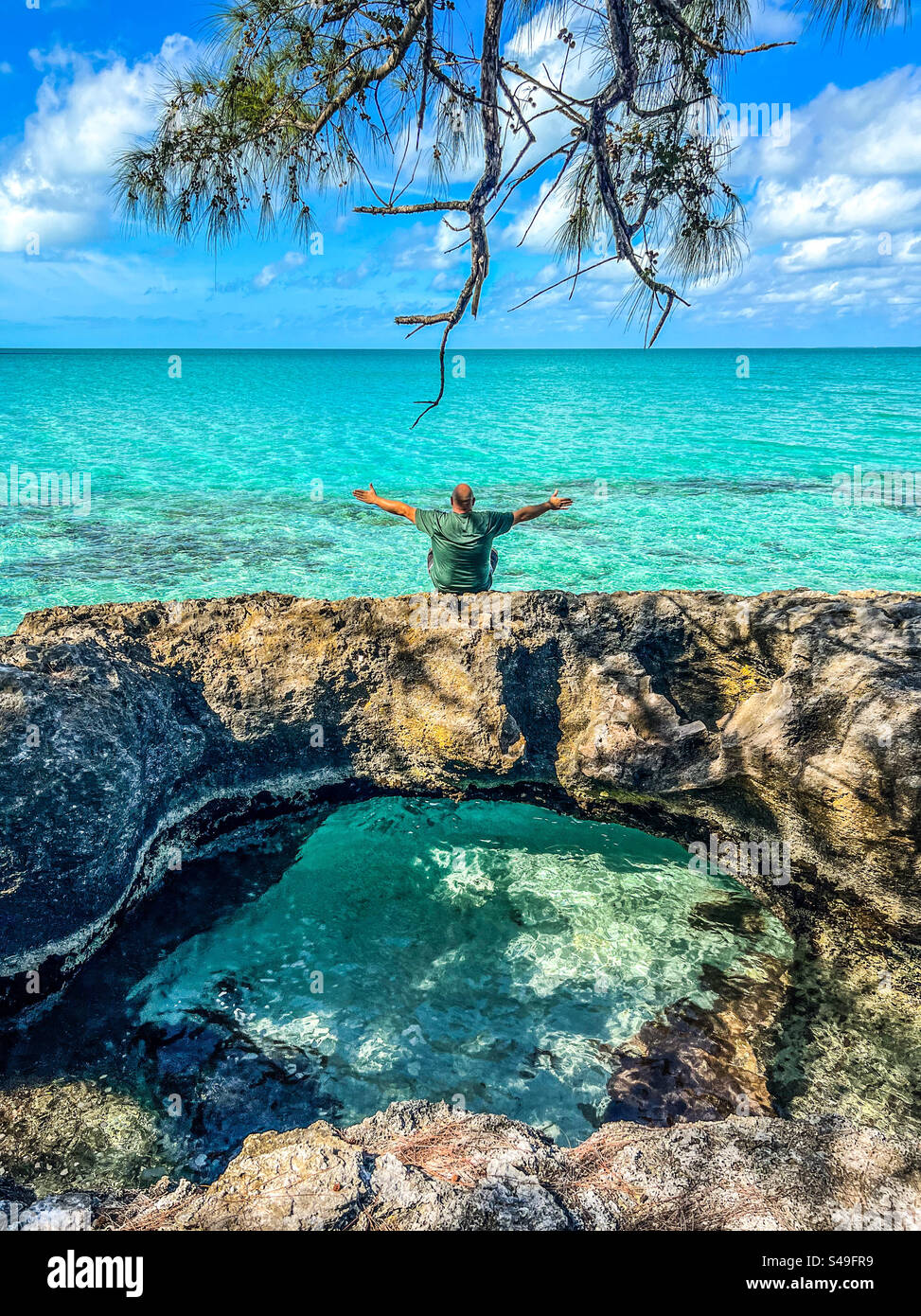A man sits next to the ocean in Tarpum Bay, Eleuthera, Bahamas on November 12, 2023. - Smartphone Captured Stock Image