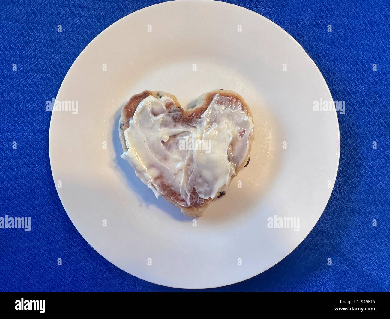 Home made heart shaped Welsh cake spread with butter on a white plate on a blue tablecloth. - Smartphone Captured Stock Image