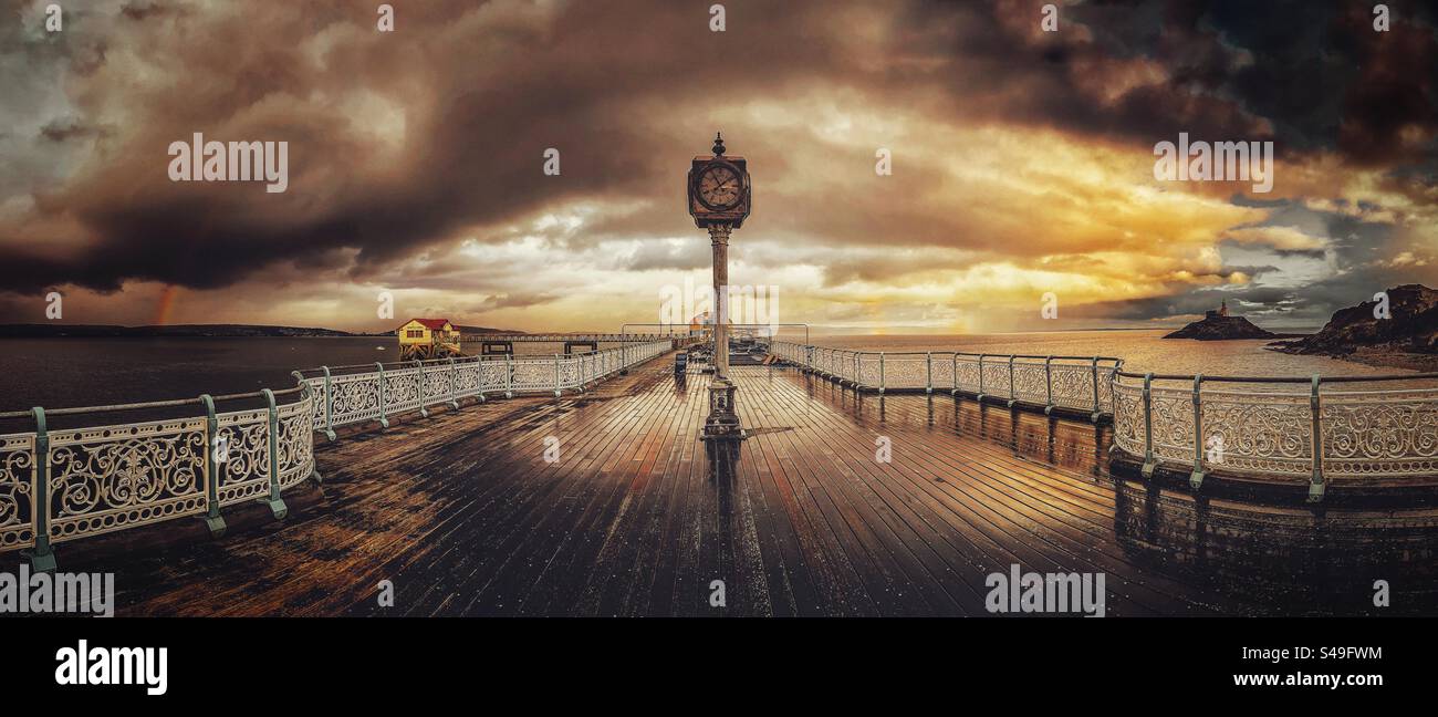 Clock on Mumbles pier, panoramic with rainbow in the background. Winter 2024, south wales, uk - Smartphone Captured Stock Image