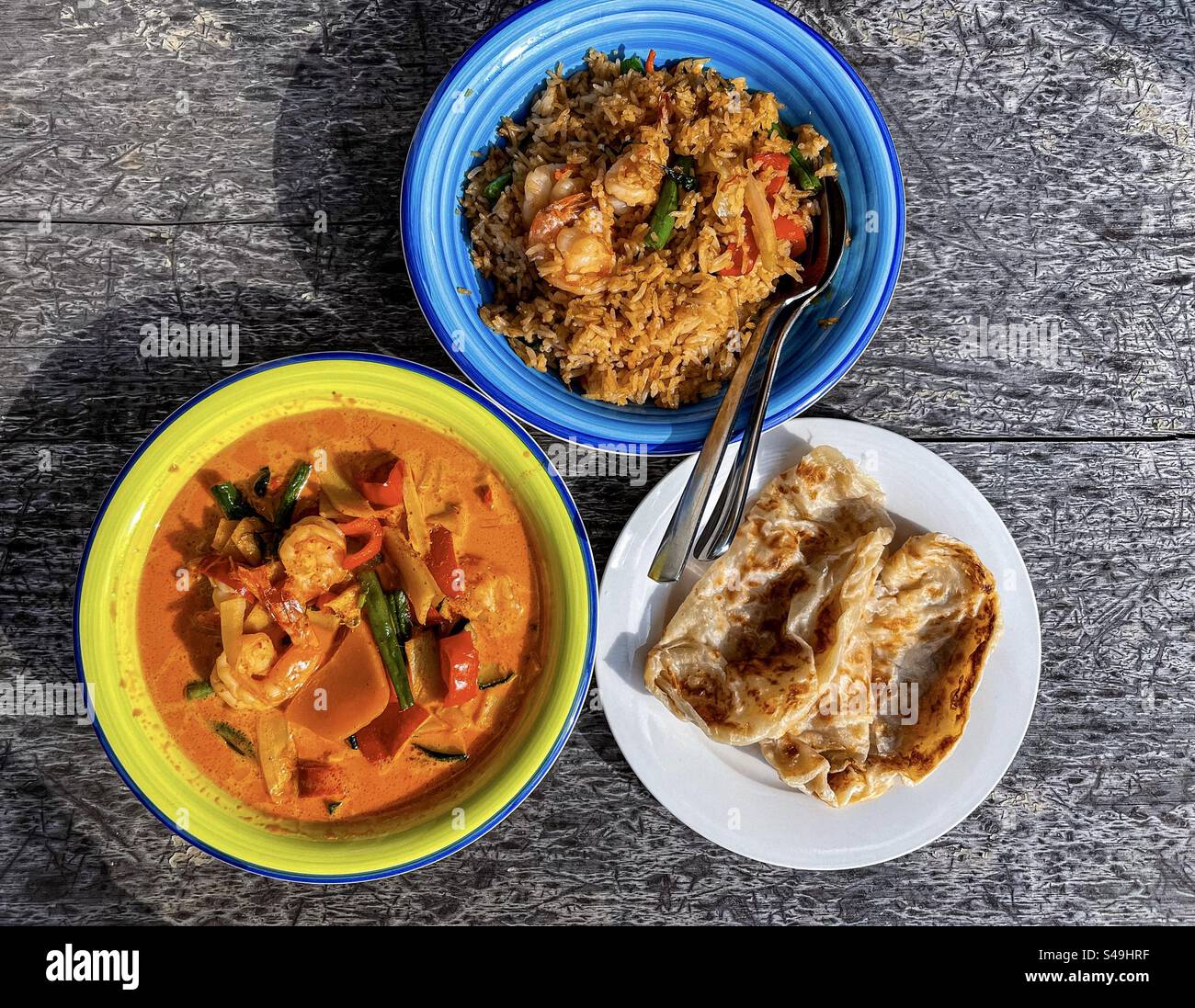 High angle view of Thai basil fried rice and Thai red curry in bowls with roti, pan-fried flatbread on plate on table. Thai cuisine. - Smartphone Captured Stock Image