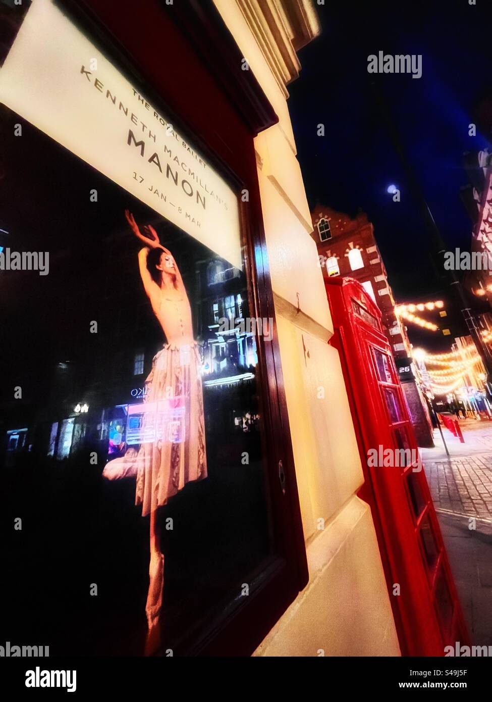 Reflections - in the glass of a poster advertising Manon at The Royal Opera House in Covent Garden with telephone box and string lights across the night sky with moon visible. London nightlife. - Smartphone Captured Stock Image