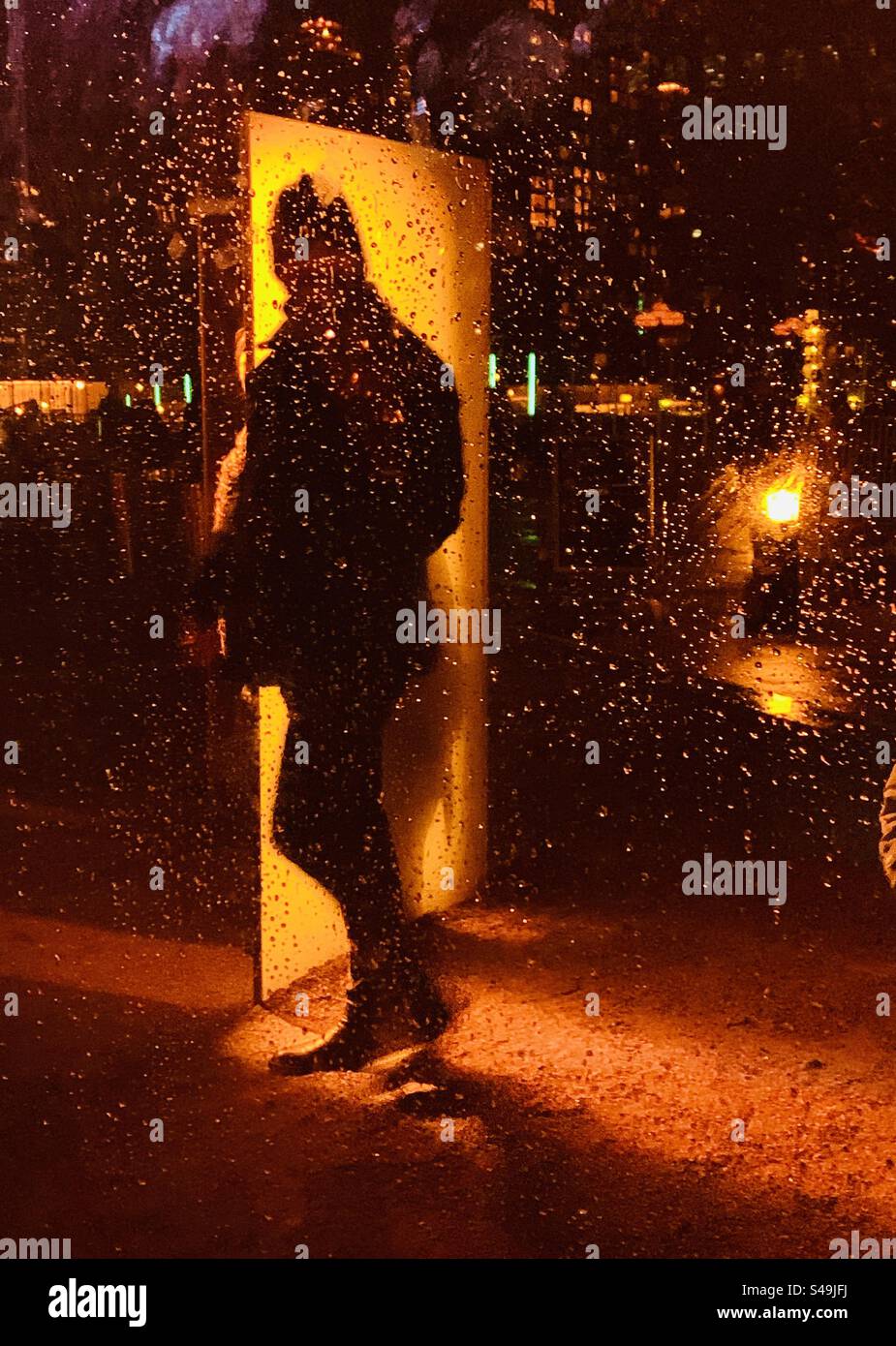Silhouette of man walking in the rain in London against bright orange background - Smartphone Captured Stock Image
