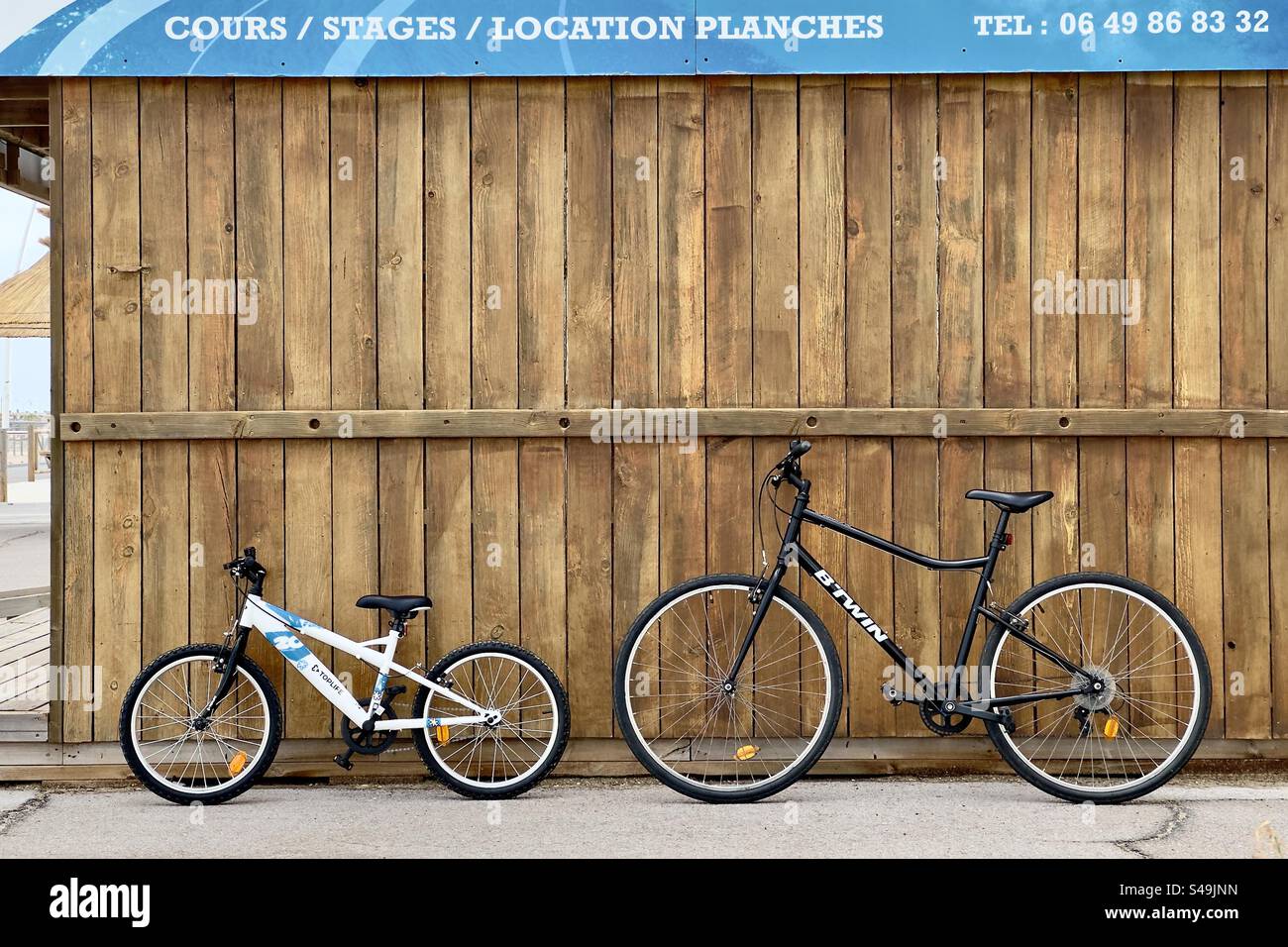 Shot of two bikes, one white kids and one black adult resting against a wooden wall. - Smartphone Captured Stock Image
