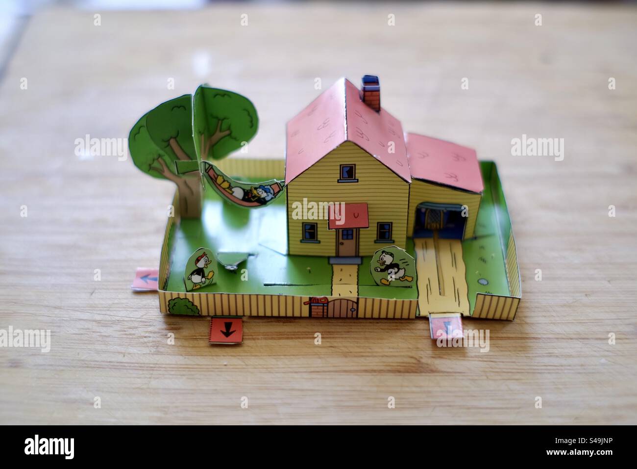 Closeup shot of a paper or cardboard animated cutout house and garden for kids resting on a wooden table. - Smartphone Captured Stock Image