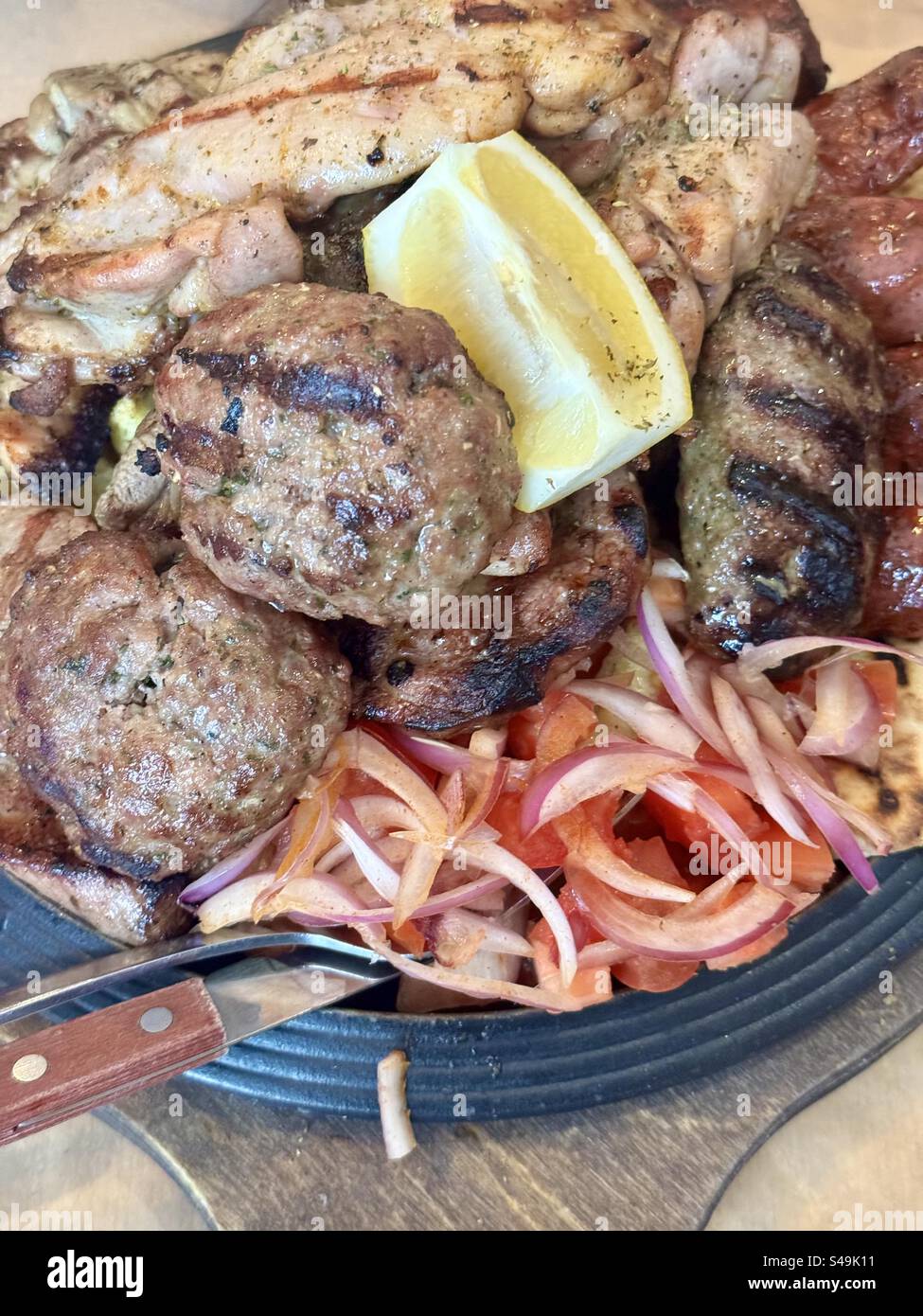 Traditional Greek grilled meat platter with lemon, onions, and tomatoes served in a rustic style. - Smartphone Captured Stock Image