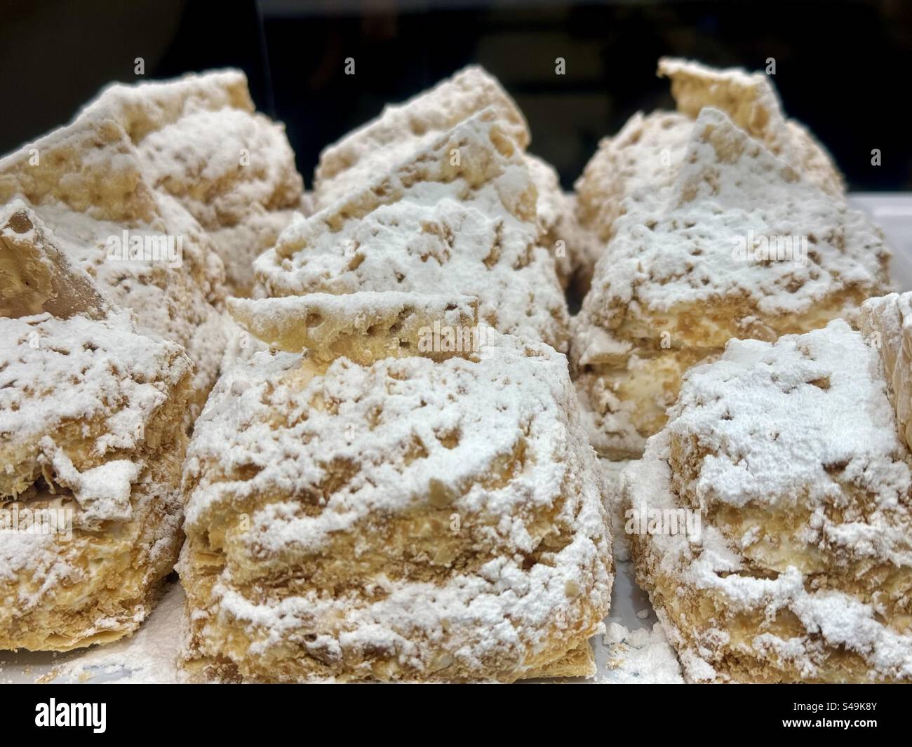 Close-up of traditional Greek sweet cakes dusted with powdered sugar, displayed in a bakery. - Smartphone Captured Stock Image