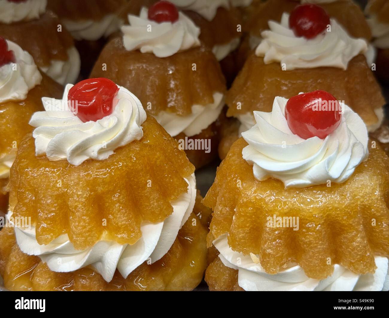 Close-up of traditional Greek sweet cakes topped with whipped cream and a cherry, displayed in a bakery. - Smartphone Captured Stock Image