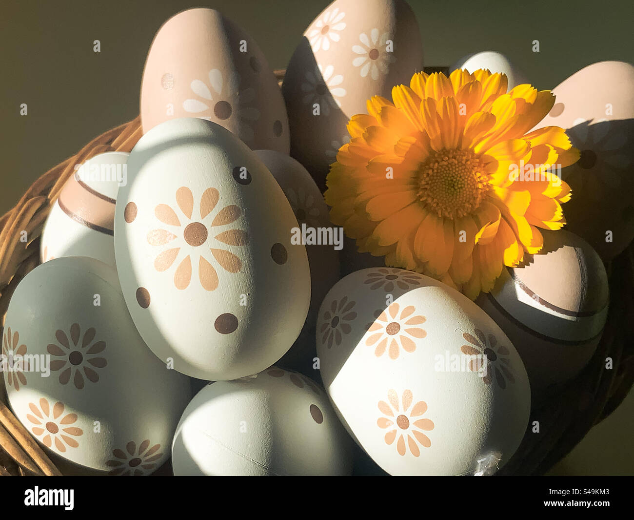 A basket of decorated eggs with a yellow pot marigold flower, under shadowy light - Smartphone Captured Stock Image