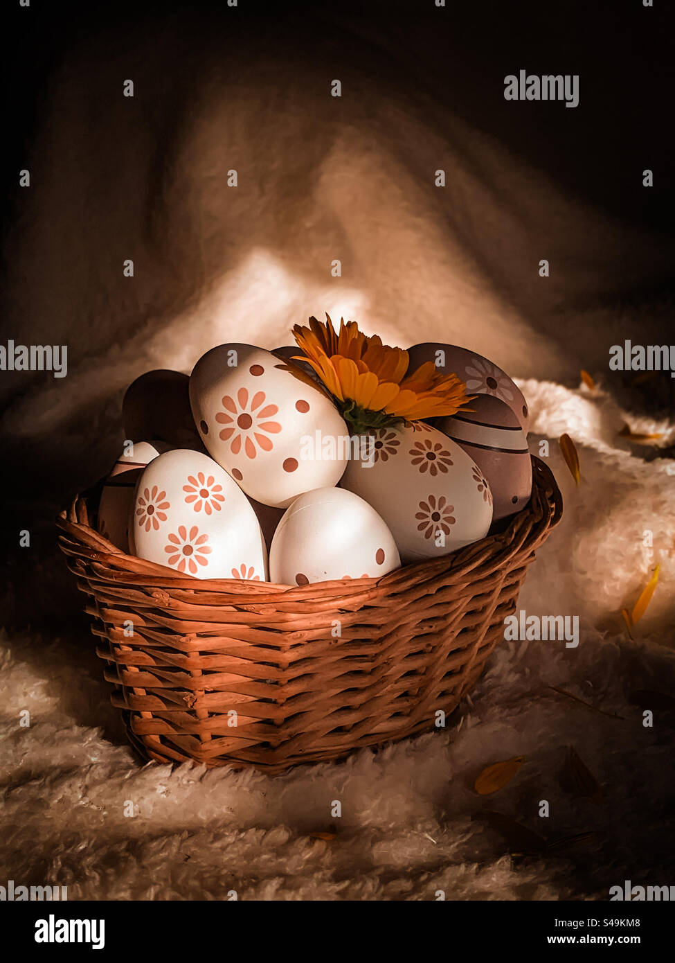 A basket of decorated eggs with a yellow flower, on a white, soft and shadowy background - Smartphone Captured Stock Image