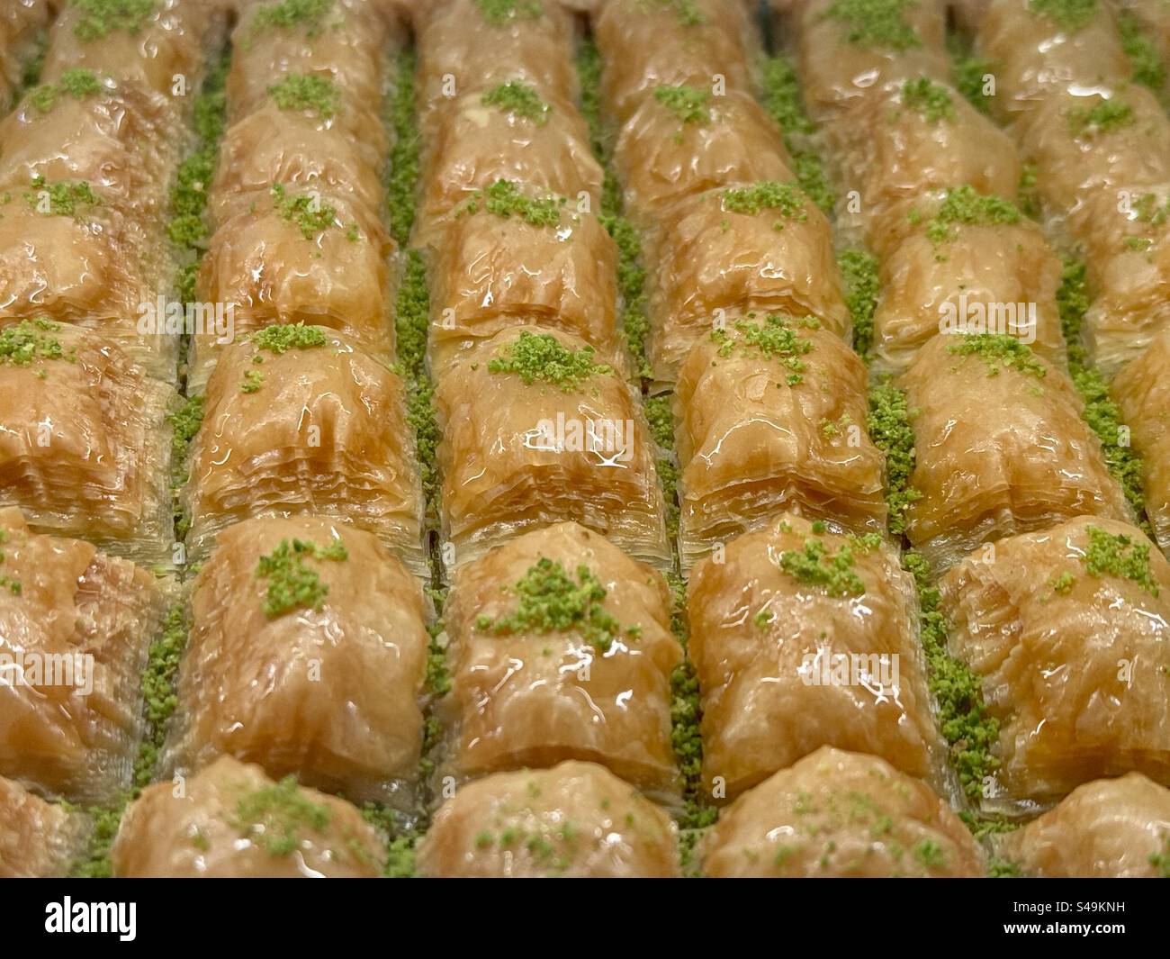 Close-up of traditional Freshly made Greek baklava pastries arranged neatly in rows, glistening with syrup and topped with crushed pistachios. - Smartphone Captured Stock Image
