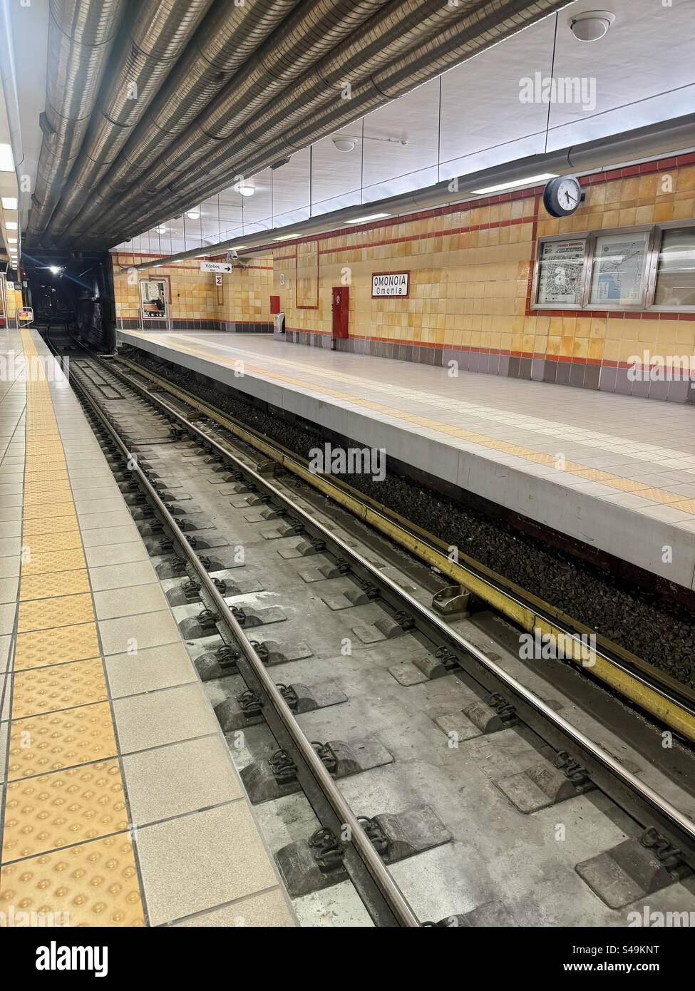 Empty platform at Omonia subway station in Athens, Greece, featuring tiled walls and overhead piping. - Smartphone Captured Stock Image