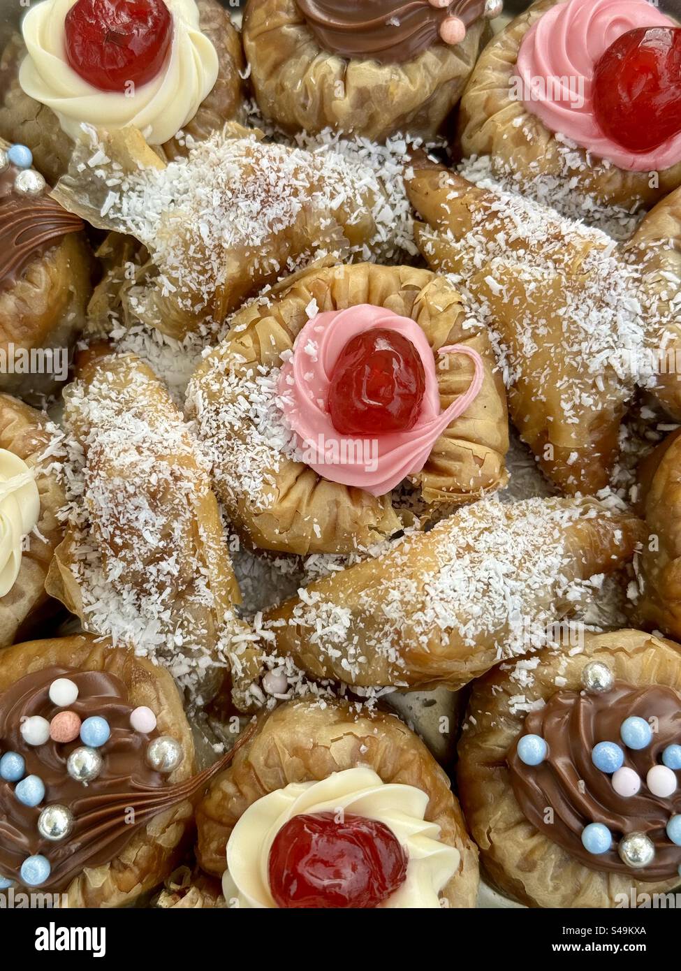 Close-up image of assorted Baklava and Saragli traditional Greek and Turkish sweets topped with cherries and coconut flakes, displayed in Athens, Gree - Smartphone Captured Stock Image
