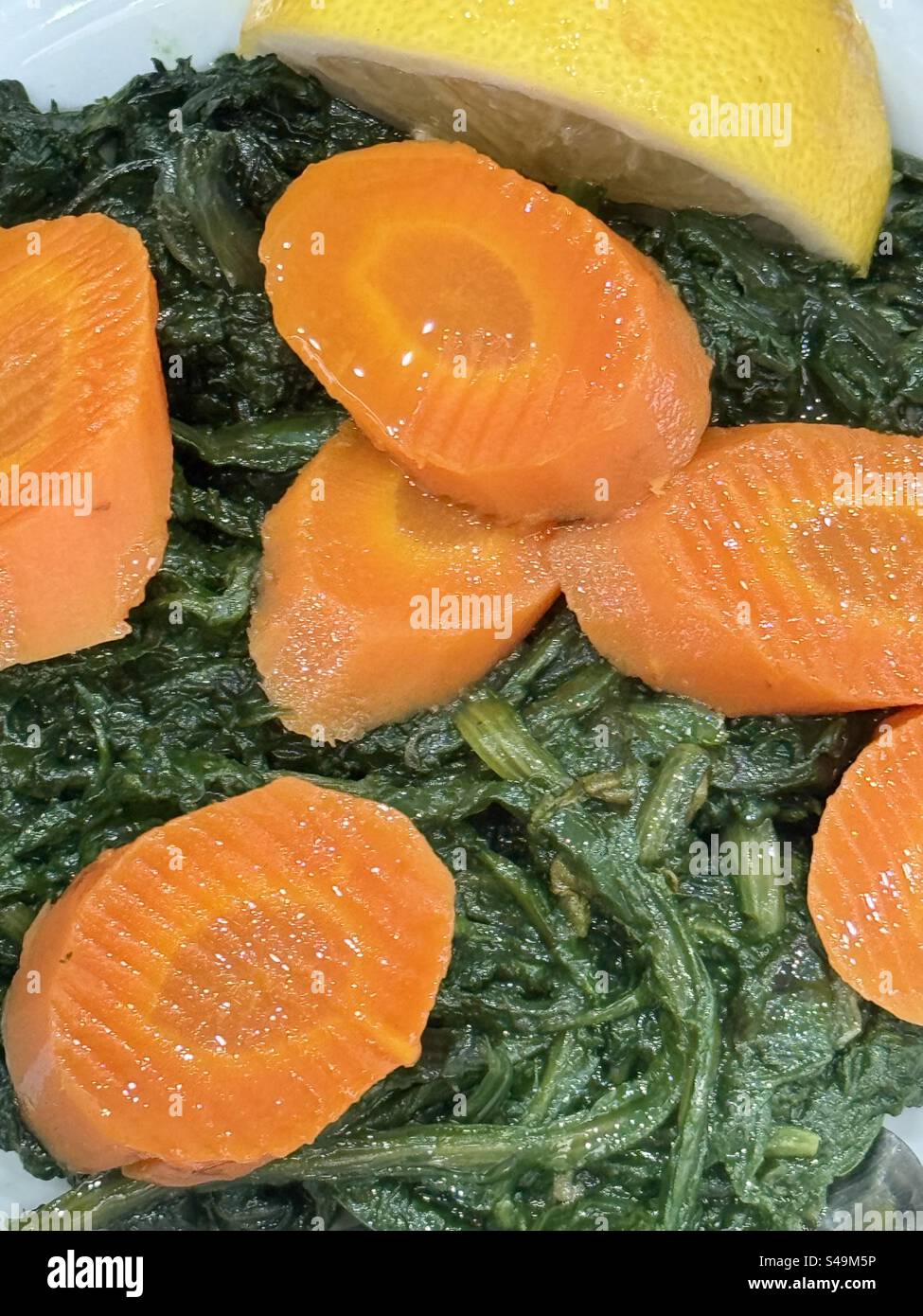 Boiled greens and sliced carrots served with a lemon wedge, a traditional healthy dish from Mediterranean cuisine. - Smartphone Captured Stock Image