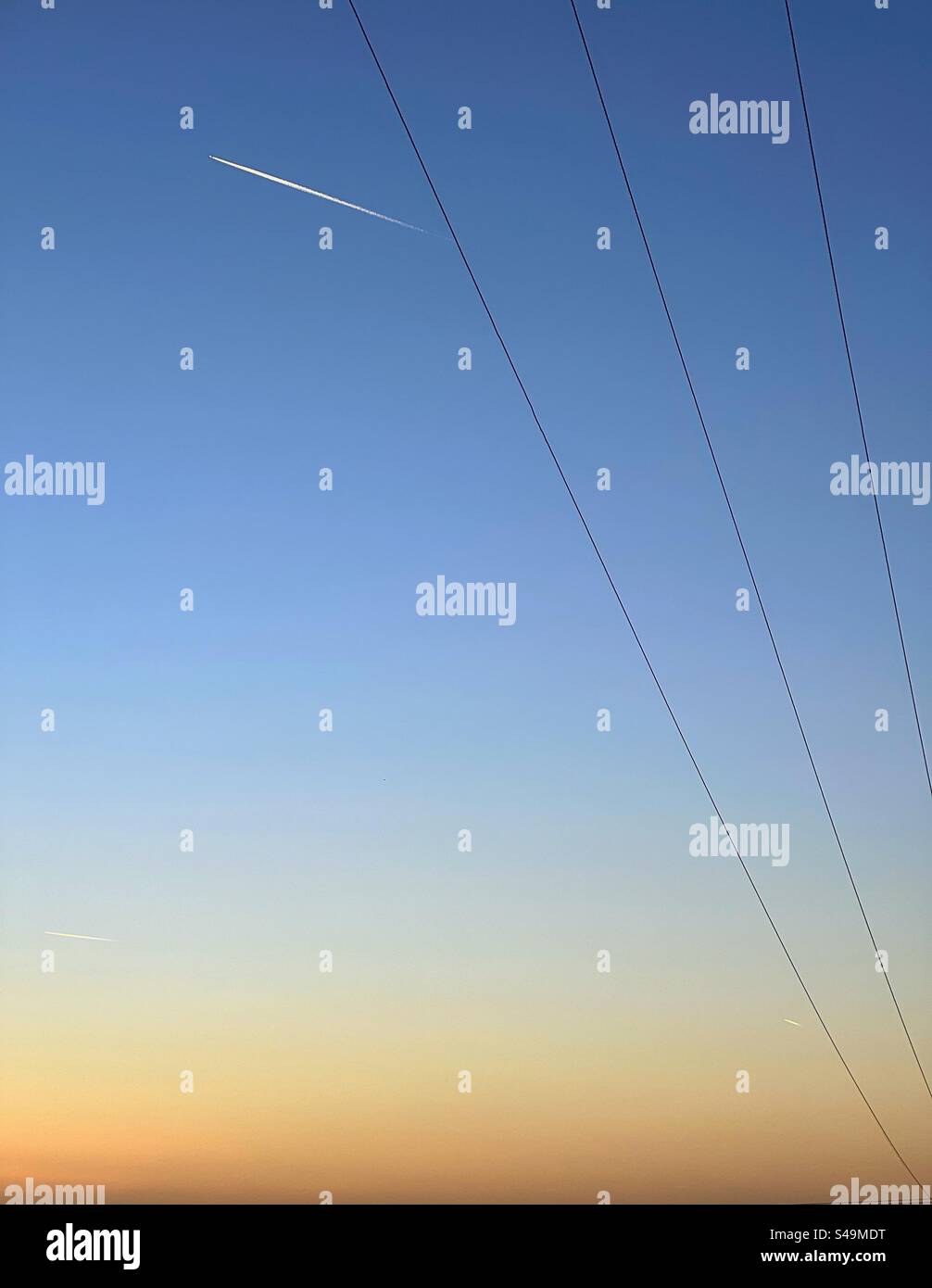 Power cables against a blue sky at sunset with vapour trail - Smartphone Captured Stock Image