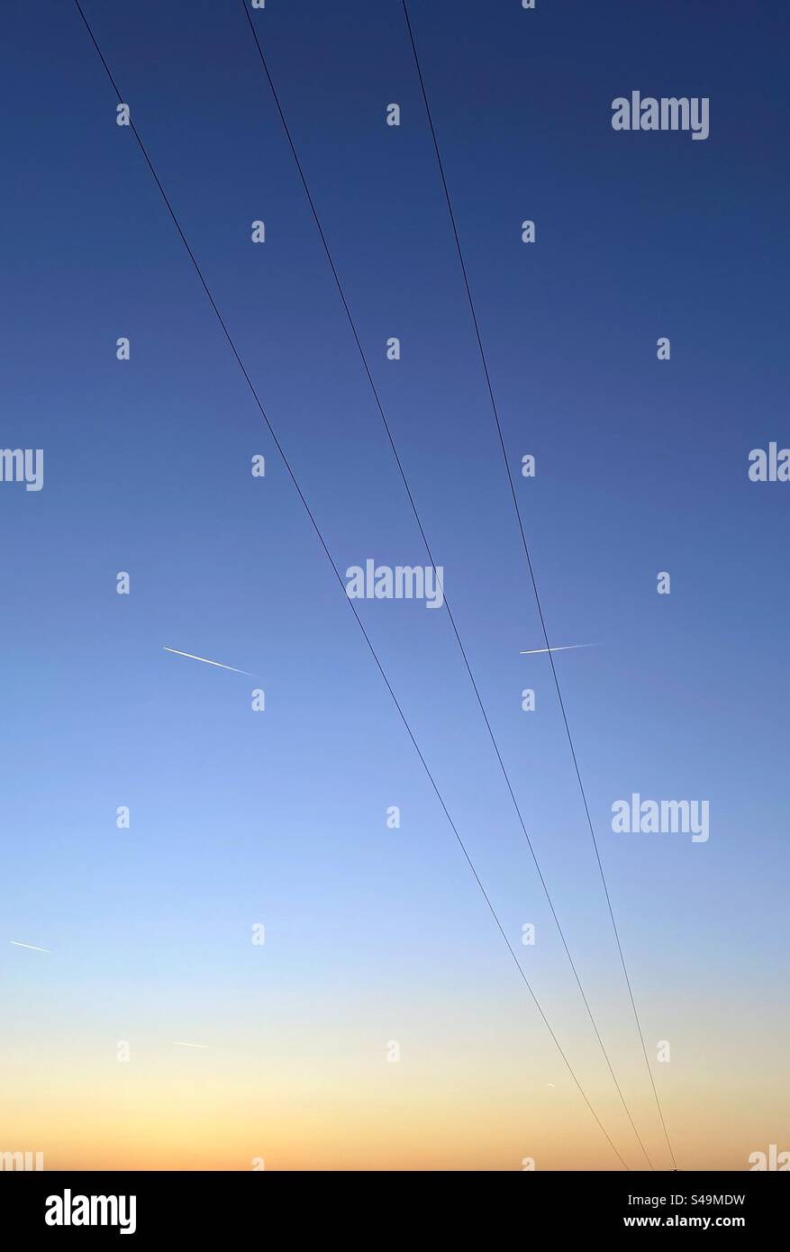 Power cables against a blue sky at sunset with vapour trails - Smartphone Captured Stock Image