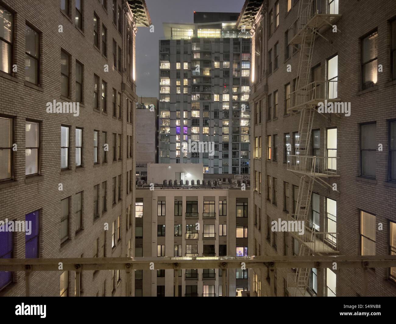 LOS ANGELES, CA, AUG 20, 2023: Night view of modern apartment building seen past the windows of a historic office building, converted to apartments in Downtown - Smartphone Captured Stock Image