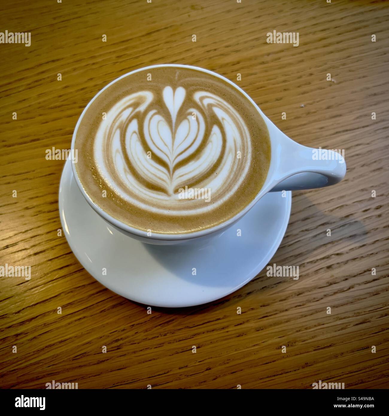 Latte coffee with attractive pattern in the cream on top, white ceramic cup on wooden table - Smartphone Captured Stock Image