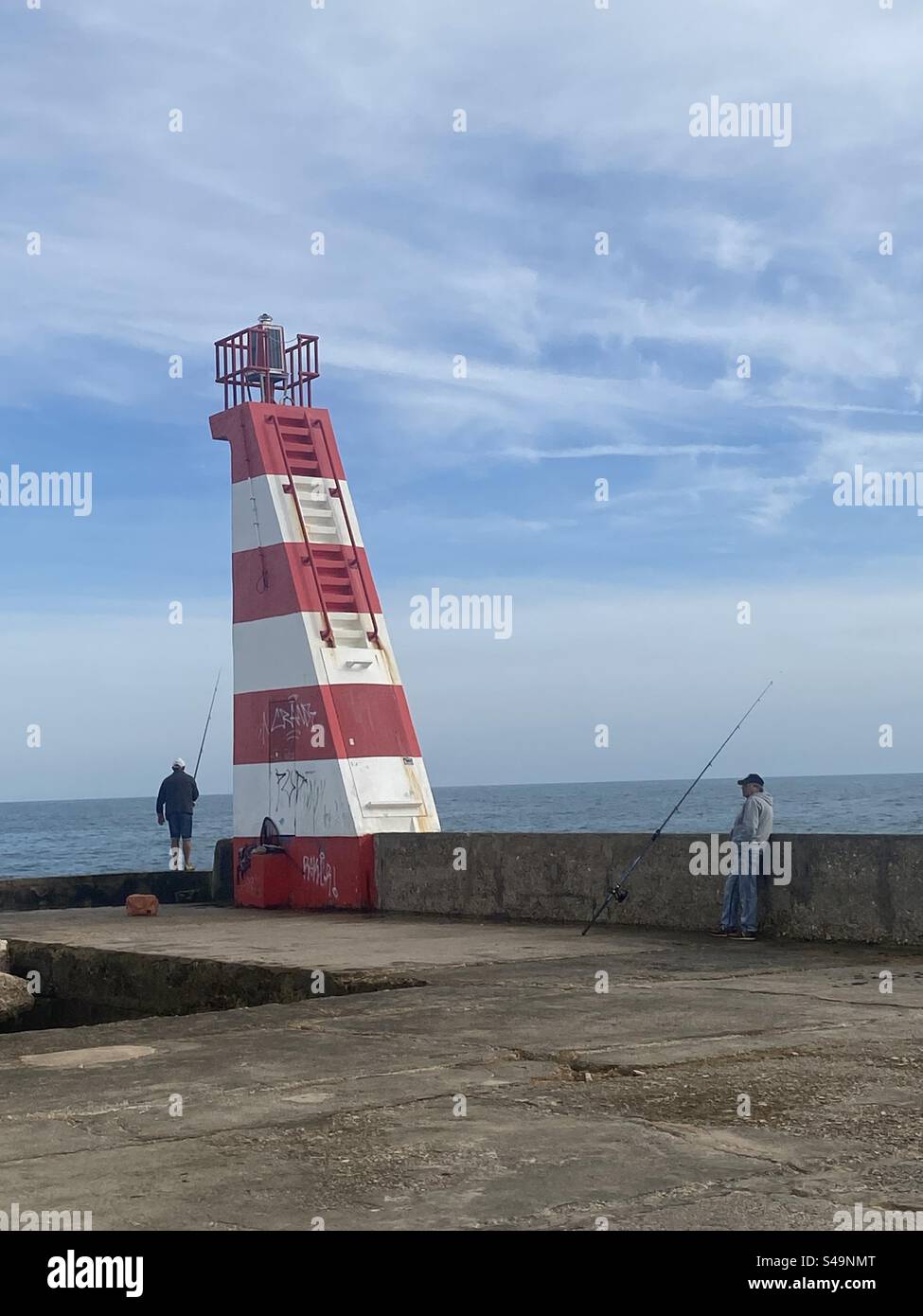 Men fishing at the entrance to the marina beside the lake house in Lagos, a Portugal - Smartphone Captured Stock Image