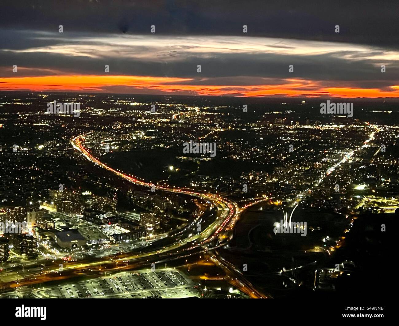 Striking orange sun setting on the horizon where they darkening evening sky meets the up with a city full of lights in this aerial view. - Smartphone Captured Stock Image