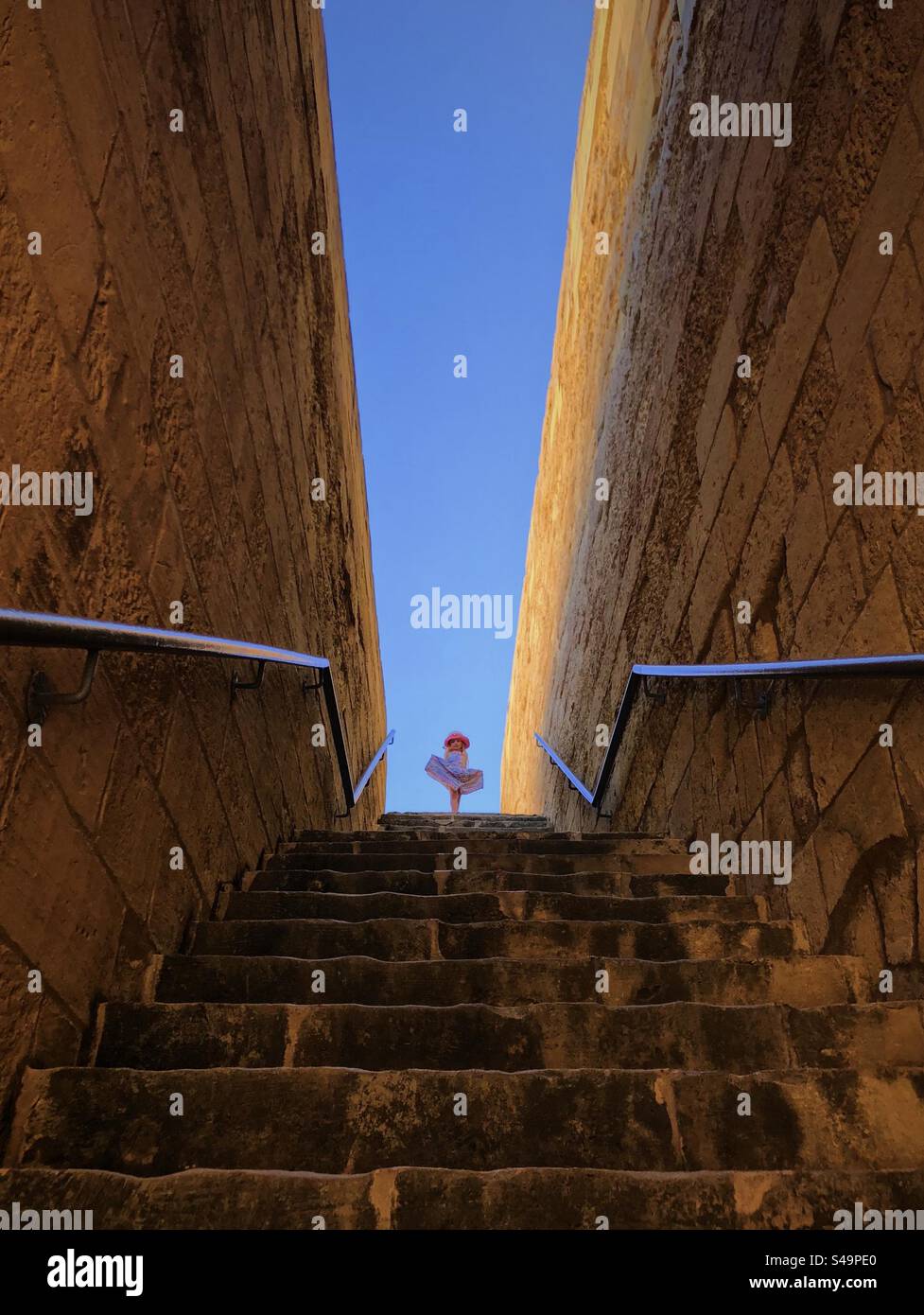 Low angle view, looking up stone staircase at little girl framed against blue sky Stock Photo