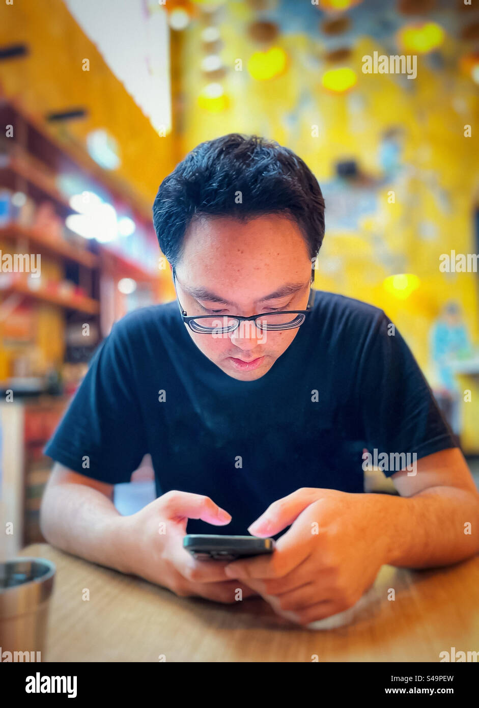 Close-up of Asian man in eyeglasses, using mobile phone at table in cafe. Wireless technology. Food and drink. - Smartphone Captured Stock Image