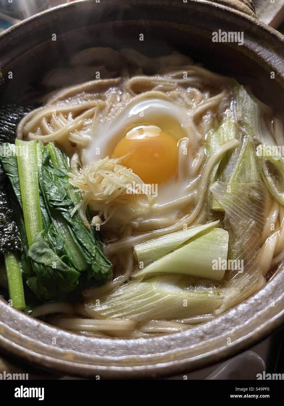 Bowl of hot Japanese nabeyaki noodles with raw egg and vegetables - Smartphone Captured Stock Image