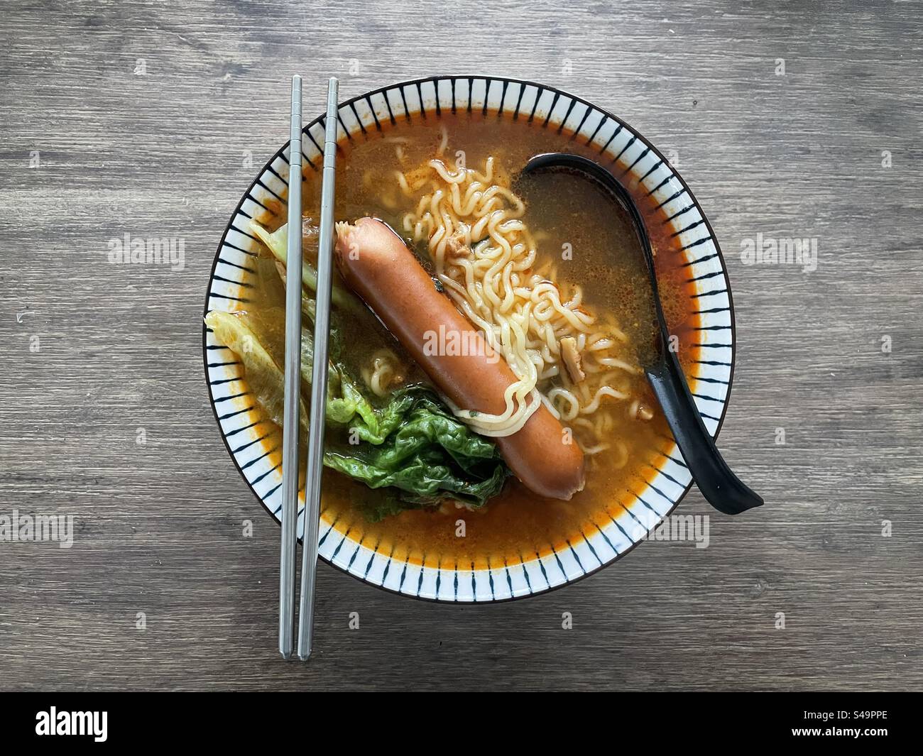 Noodle soup with sausage chili and salad top view with 2 chopsticks in metal steel texture material and a black plastic spoon do drink this snack meal lunch diner food - Smartphone Captured Stock Image