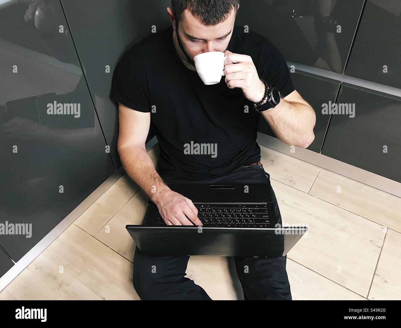 Young man drinking coffee and using laptop at home - Smartphone Captured Stock Image