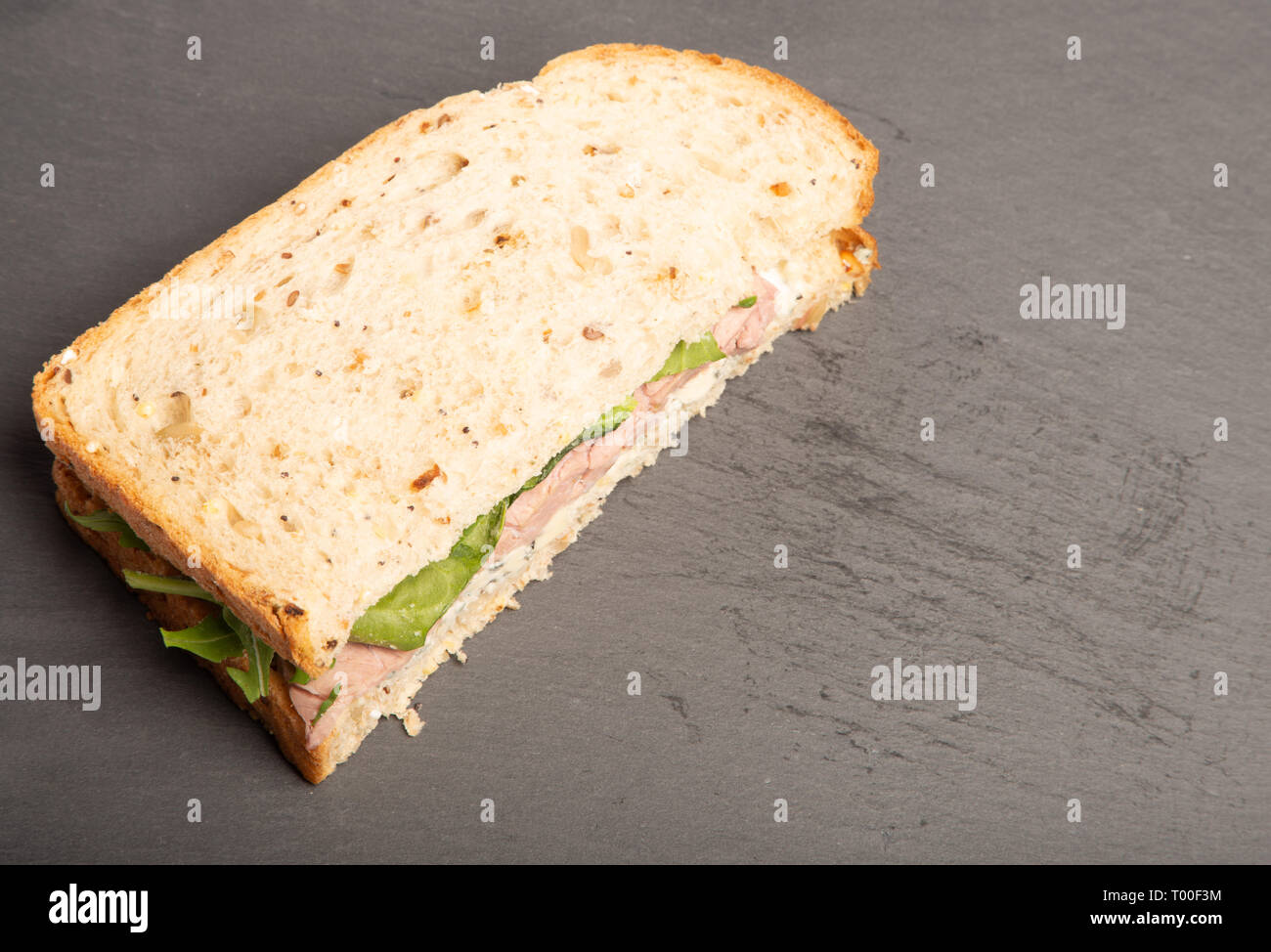 whole grain bread sandwich of steak, Stilton and spinach. delicious lunch time meal. organic with no single use wrapping, on a slate grey surface. Stock Photo