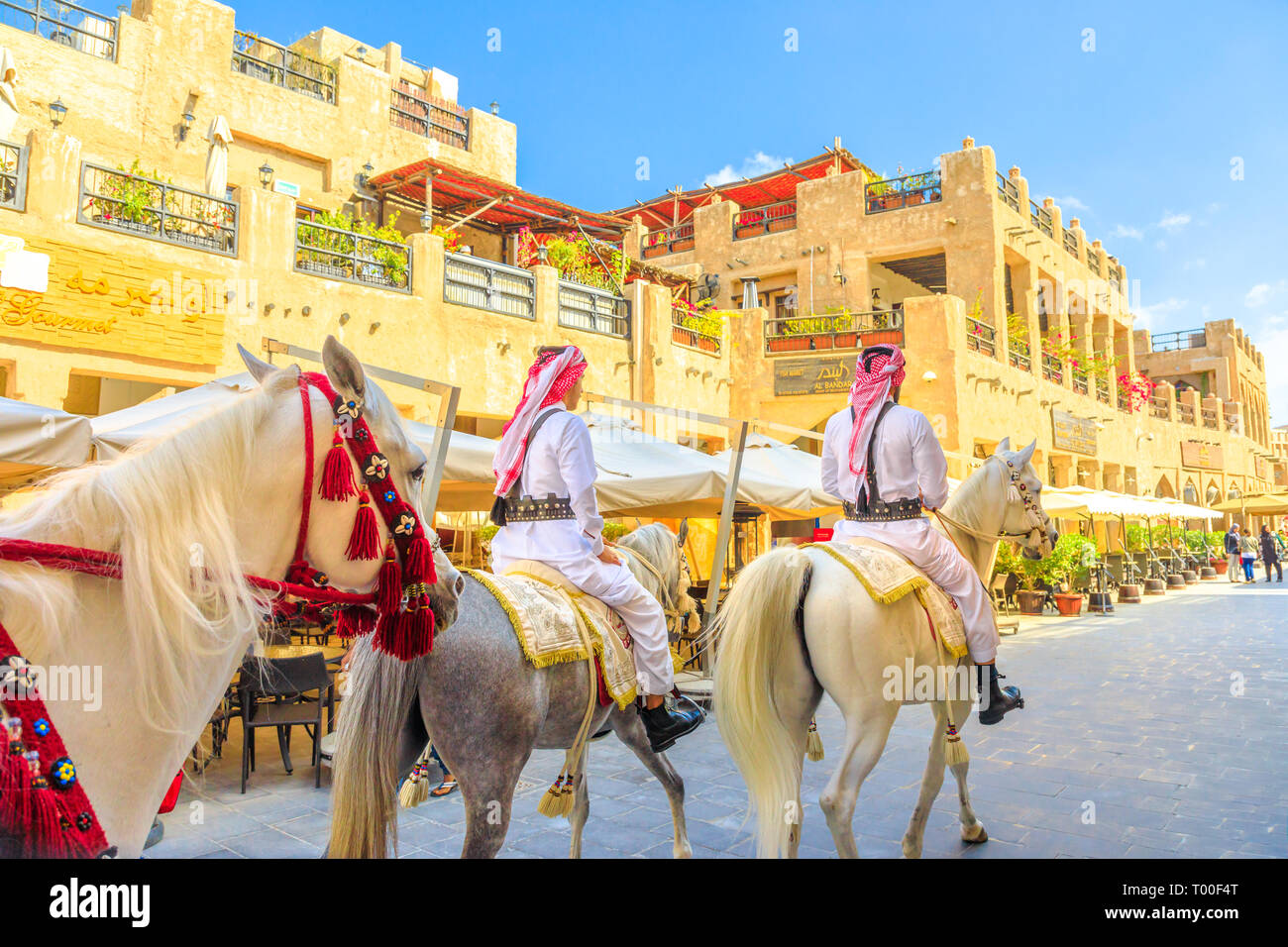 Doha, Qatar - February 20, 2019: heritage Police Officers in traditional 1940s Qatari uniform at old Souq Waqif riding white Arabian Horses on Stock Photo