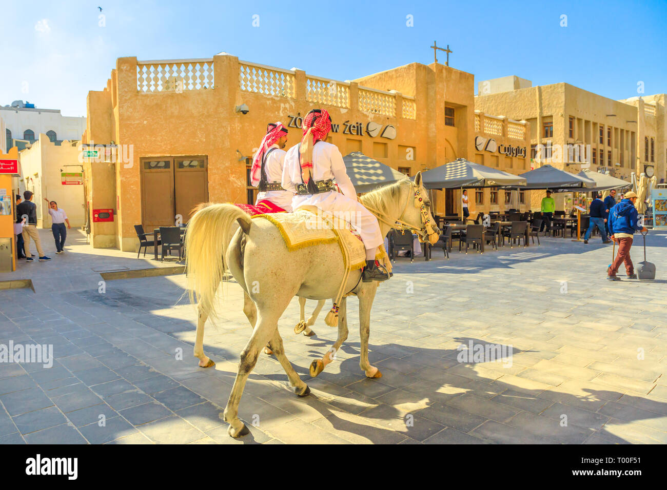 Doha, Qatar - February 20, 2019: Police on horse in traditional clothes at old Souq Waqif riding white Arabian Horses on pedestrian road. Popular Stock Photo