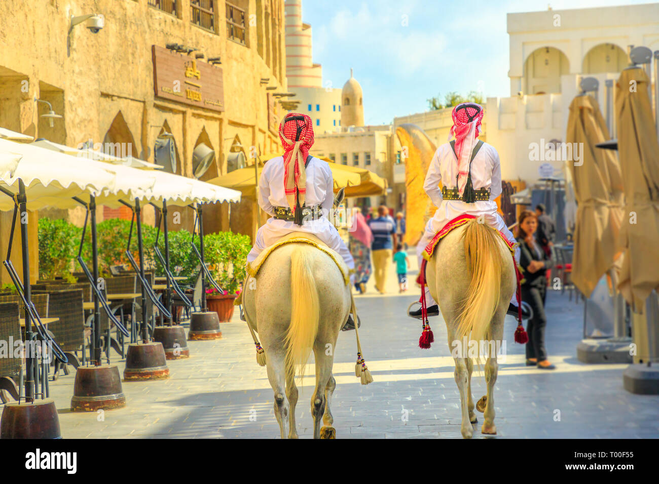 Doha, Qatar - February 20, 2019: back of heritage Police Officers in traditional 1940s Qatari uniform at old Souq Waqif riding white Arabian Horses on Stock Photo