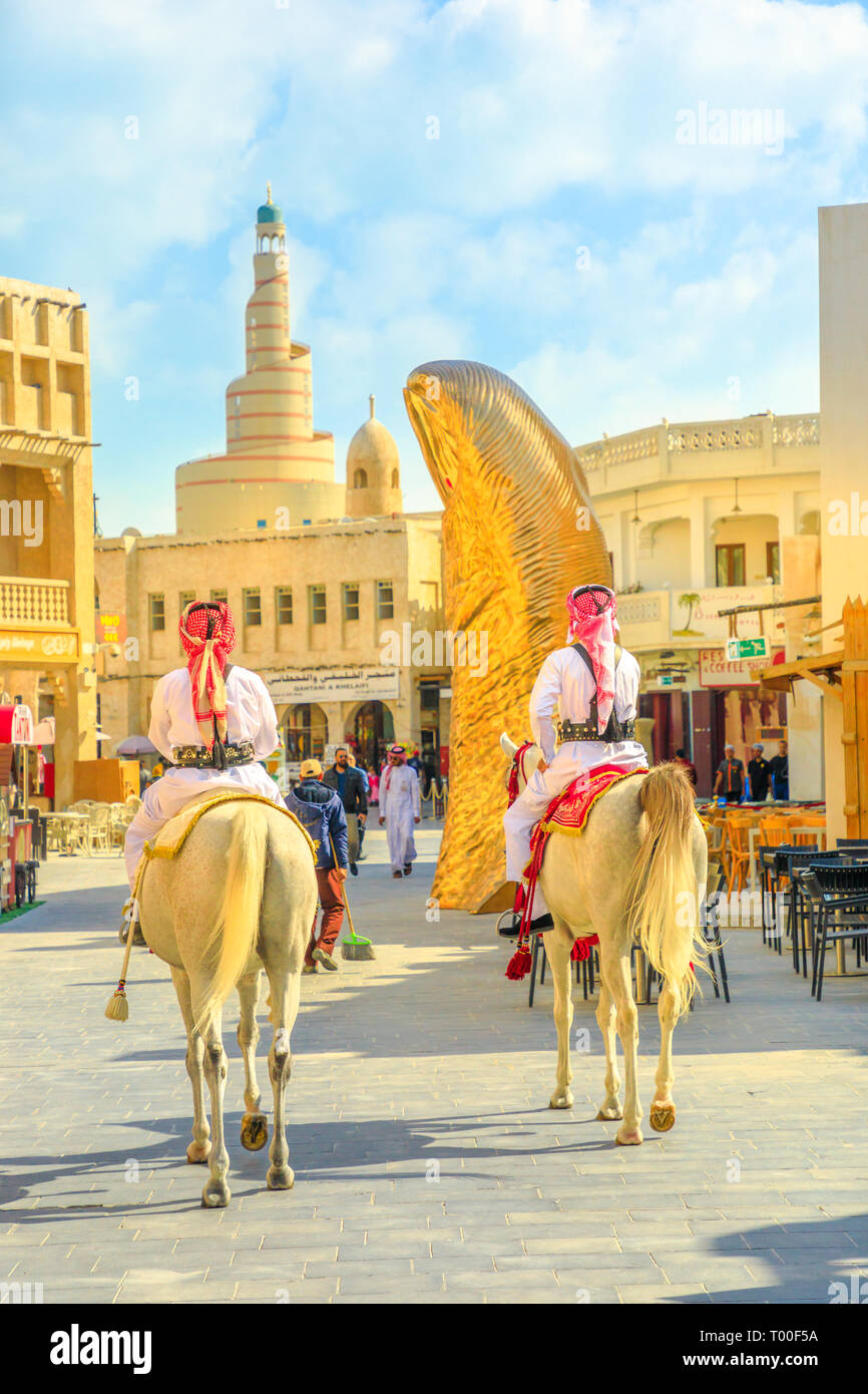 Doha, Qatar - February 20, 2019: two police officers riding white Arabian horses at Souq Waqif market. Fanar Islamic Cultural Center with Spiral Stock Photo