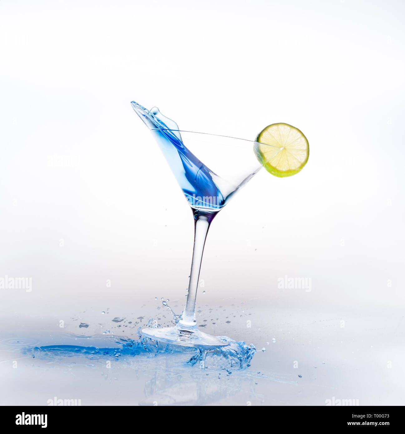 Good time party concept with Blue Curacao cocktail drink in martini class with lemon spilling and splashing against white background Stock Photo
