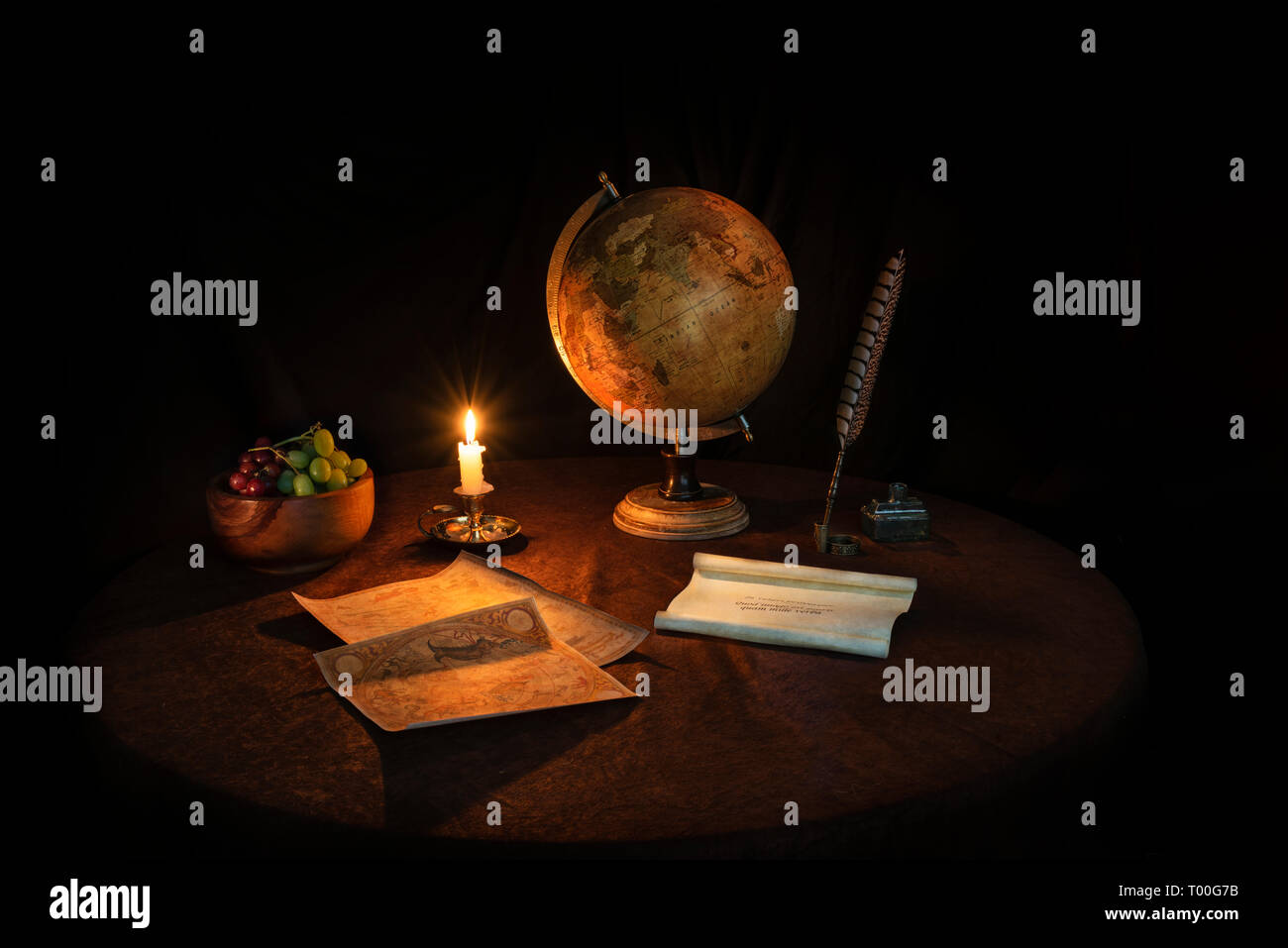 Still Life by candlelight with globe quill pen vellum scroll and fruit bowl Stock Photo