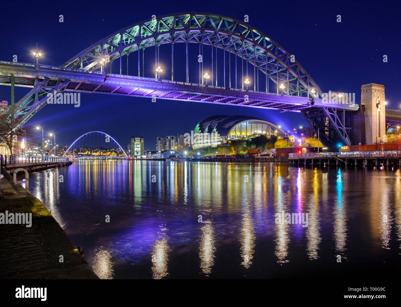After dark river Tyne bridges between Newcastle Gateshead spanned by the Tyne Bridge and Millennium Bridge showing the city lights at night. Stock Photo