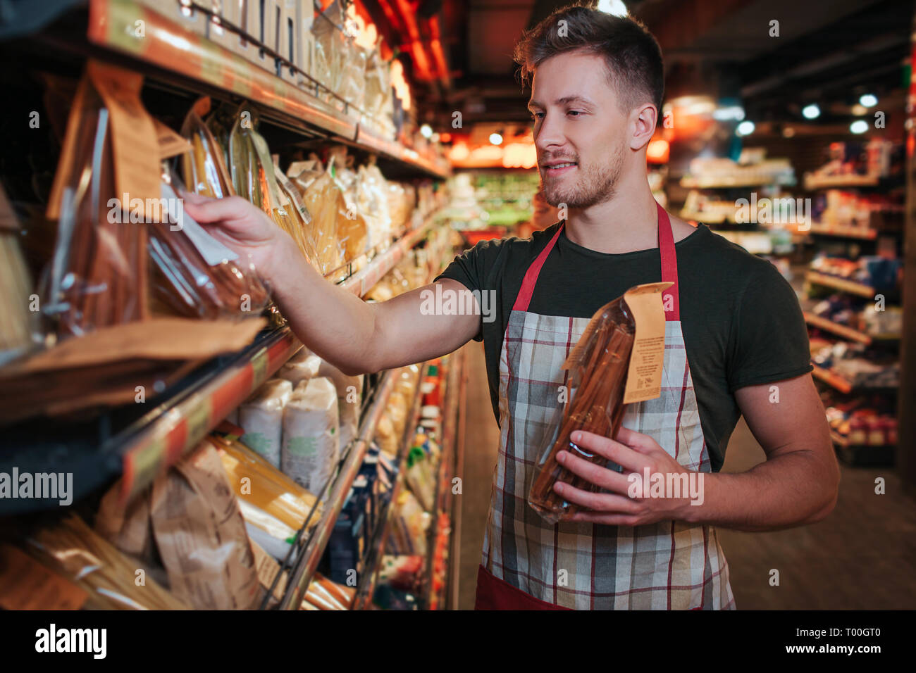 Young man stand at pasta shelf in grocery store. He put packaging on it