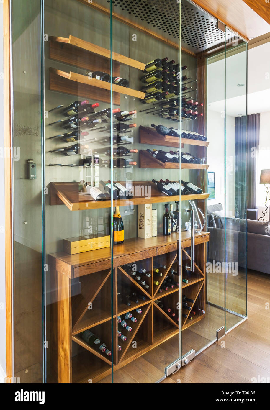 Clear glass constructed wine cellar with wooden shelves and racks filled with bottles inside a luxurious contemporary bungalow style home Stock Photo