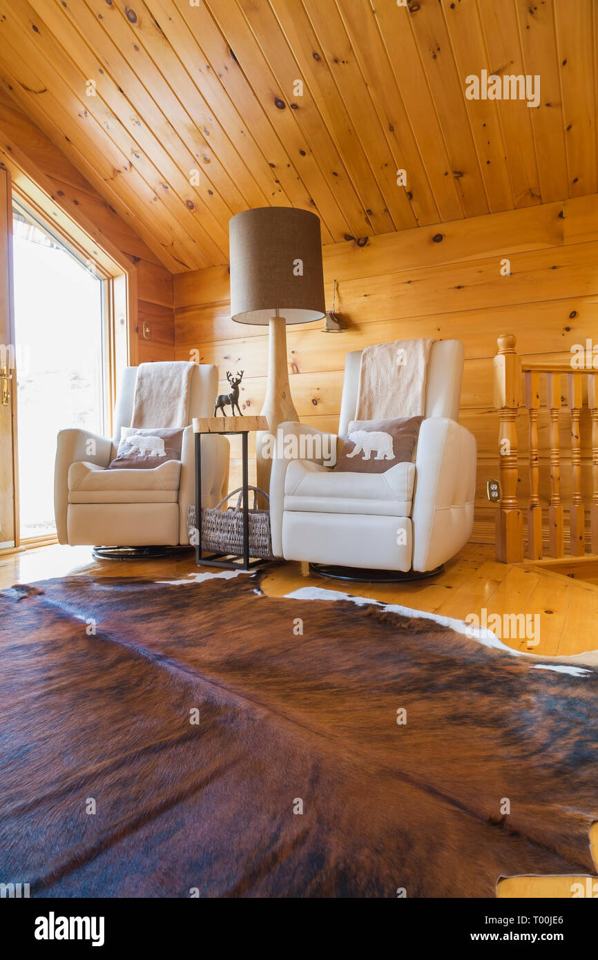 Cream leather reclining chairs with tall wooden base floor lamp and cowhide rug on upstairs floor inside a piece sur piece Eastern white pine log home Stock Photo