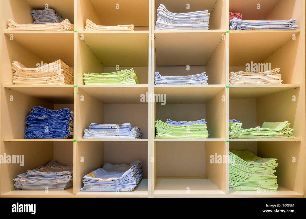 Interior of white plastic cabinet or clothing open wardrobe with stacked piles of clean colorful linen on shelves. Furniture design, hotel, hospital o Stock Photo