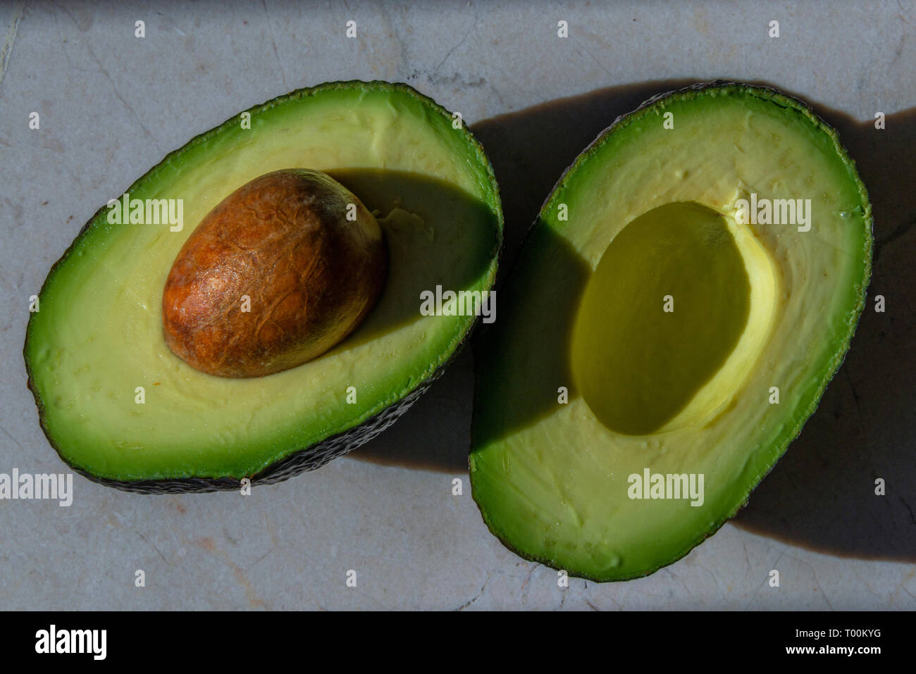 A perfectly ripe Avocado fruit, with seed, cut in two ready to scoop. The avocado belongs to the genus Persea in the Lauraceae family. Stock Photo