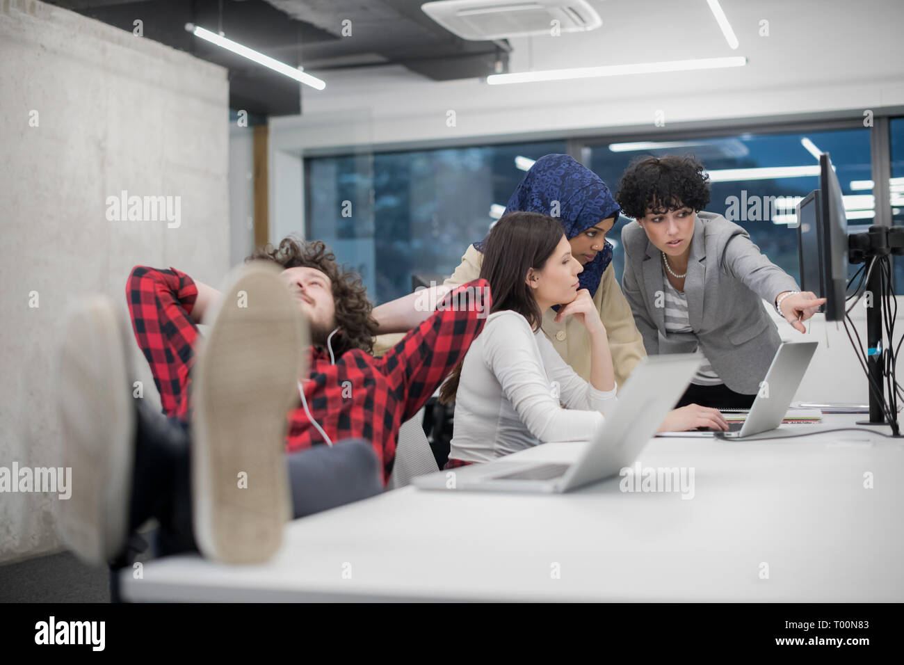 young software developer resting with legs on desk while his multiethnics business team writing programming code in the background at startup office Stock Photo