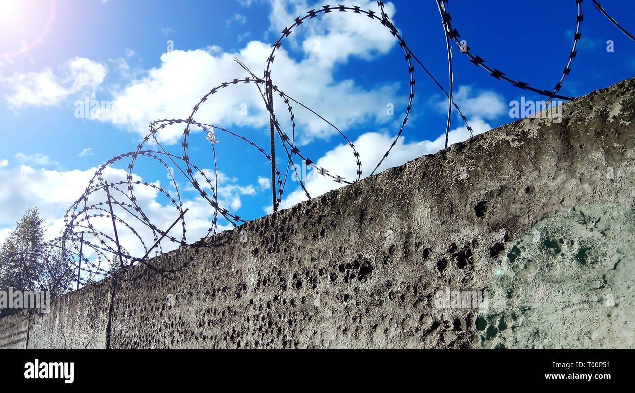 Barbed wire on a dark fence. Against a blue sky with clouds Stock Photo ...